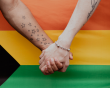A couple hold hands in front of a LGBTQ+ flag