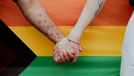 A couple hold hands in front of a LGBTQ+ flag