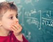 Cognition: Little boy looks confused at equation on a blackboard