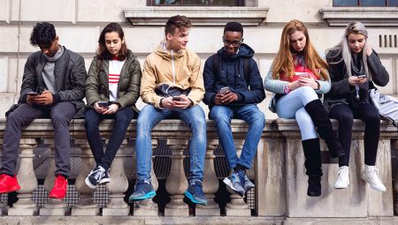 Teenagers sit on a wall and check their social media