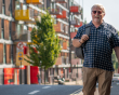 Older male walking down an empty street. He's carrying a backpack.