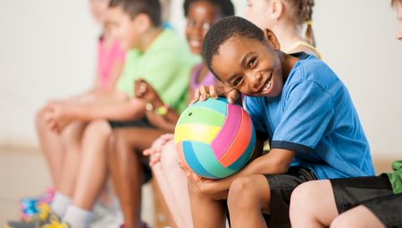 Child sits with a football in PE class