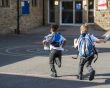 Two young boys in school uniform running in a playground with backpacks on