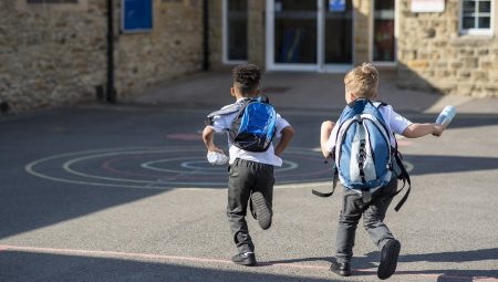 Two young boys in school uniform running in a playground with backpacks on
