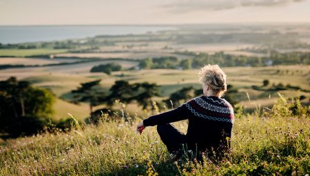 Woman sitting on a hill looking out over a view of fields and woods