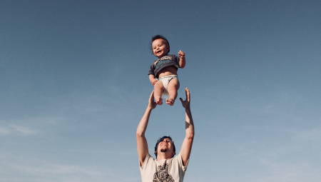 Toddler being thrown up in the air by his dad standing below ready to catch him
