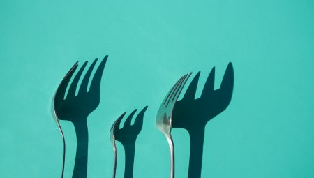 Three forks casting a shadow on a green wall