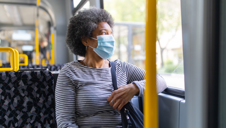 Woman wearing a face mask sits on a bus looking out the window
